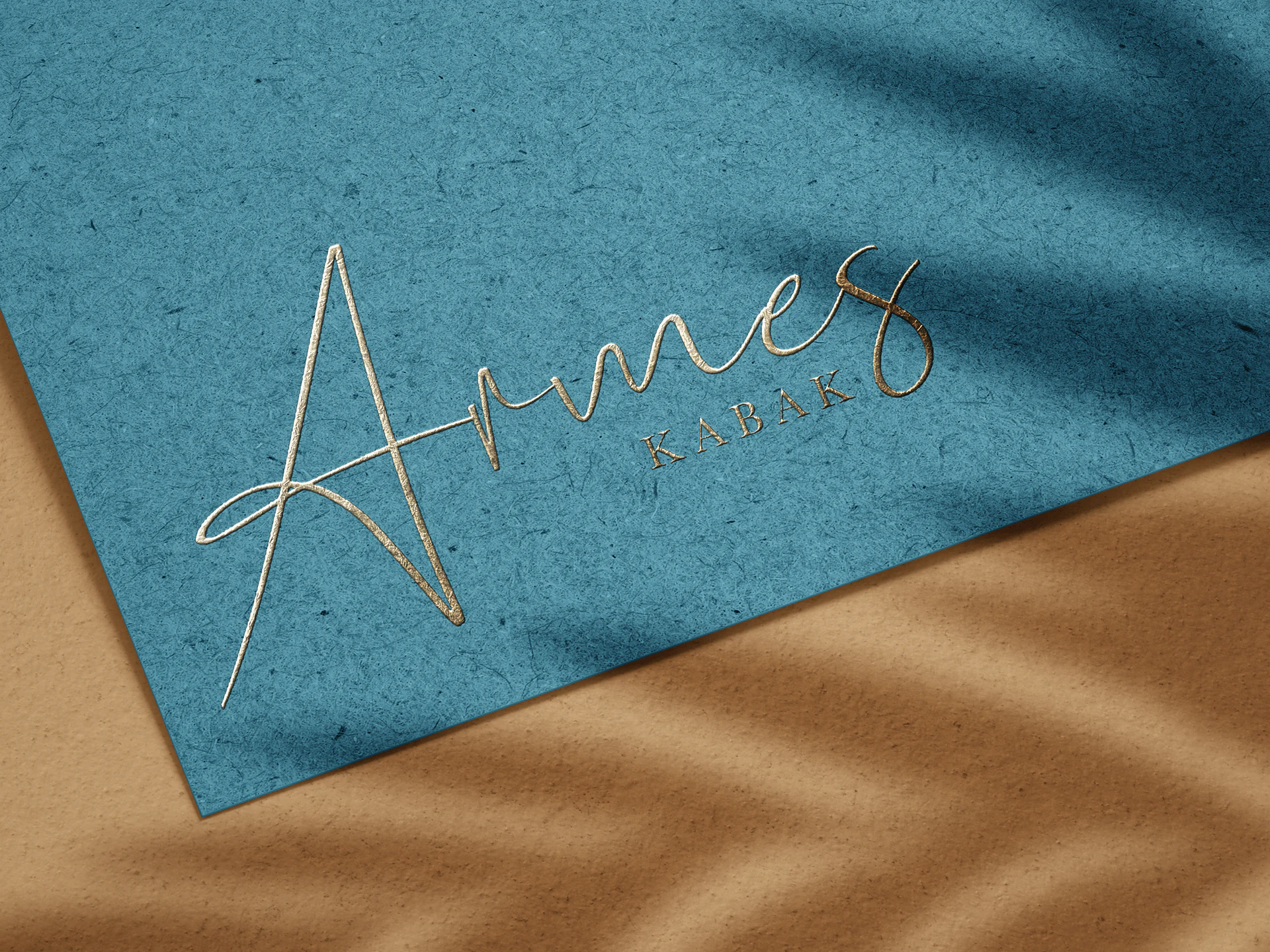 Gold Armes Kabak hotel logo with script and serif lettering on textured teal paper