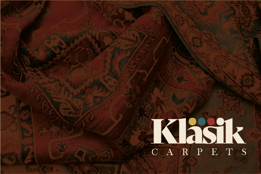 Cream Klasik Carpets logo with four coloured dots on a dark red carpet photograph